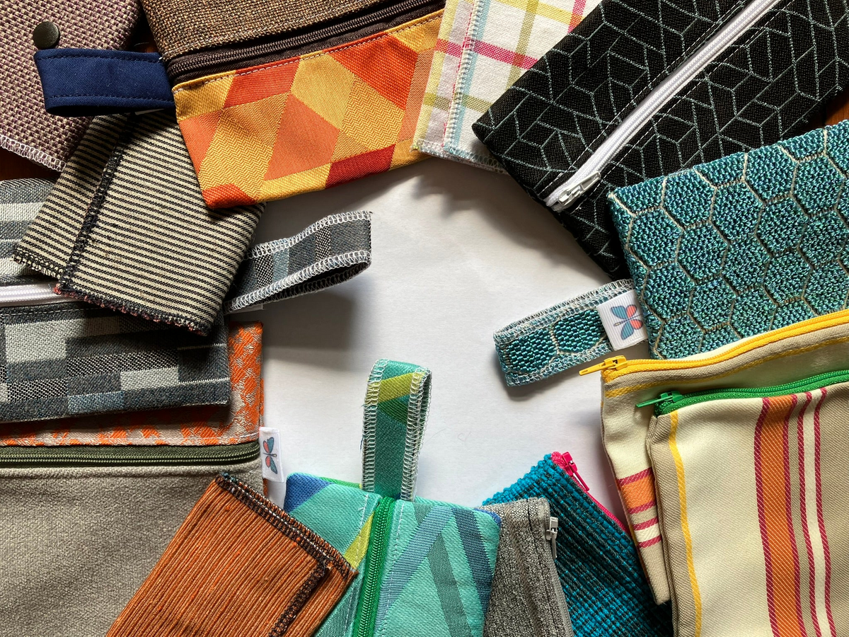 A collection of colorful fabric zippered pouches and small bags arranged in a circle on a white surface, showcasing various patterns including stripes, geometric prints, and textured fabrics.